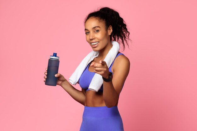 Mulher afro-americana esportiva segura garrafa de água apontando o dedo para o estúdio