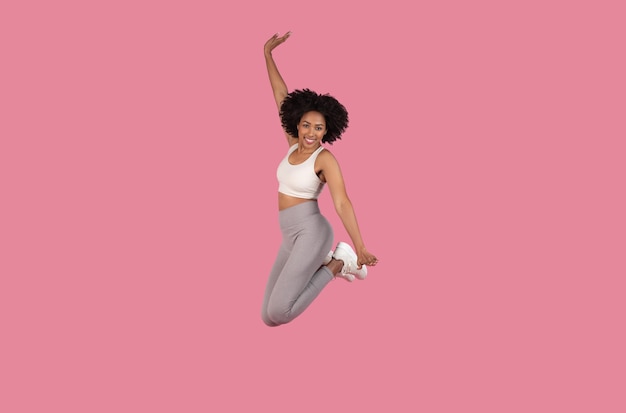 Mulher afro-americana exuberante a saltar em trajes de fitness.