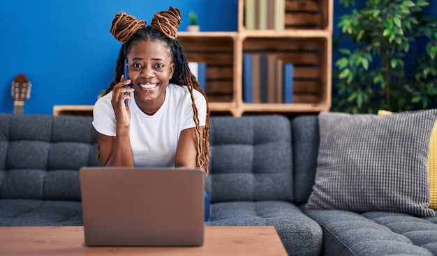 Mulher afro-americana falando em smartphone usando laptop em casa