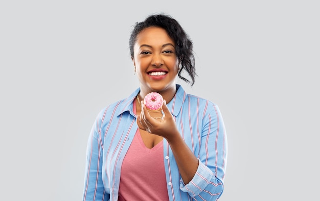 Mulher afro-americana feliz a comer um donut rosa.