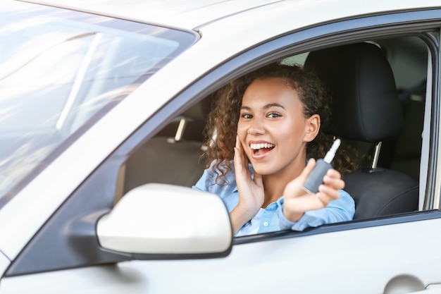 Mulher afro-americana feliz com a chave sentada em um carro novo