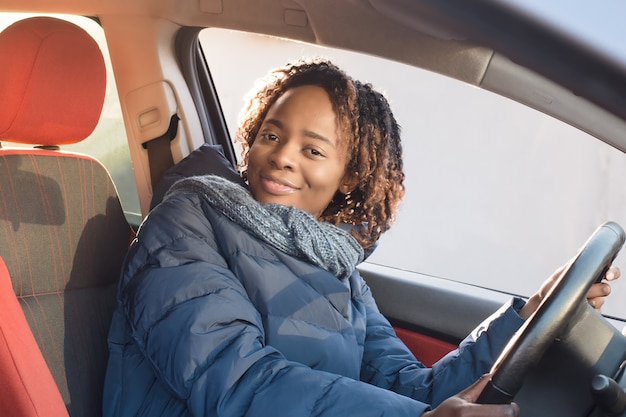 Mulher afro-americana feliz com um casaco, dirigindo o carro dela