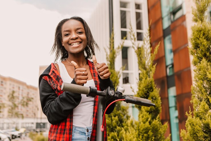 Foto mulher afro-americana feliz e sorridente com patinete elétrico na cidade