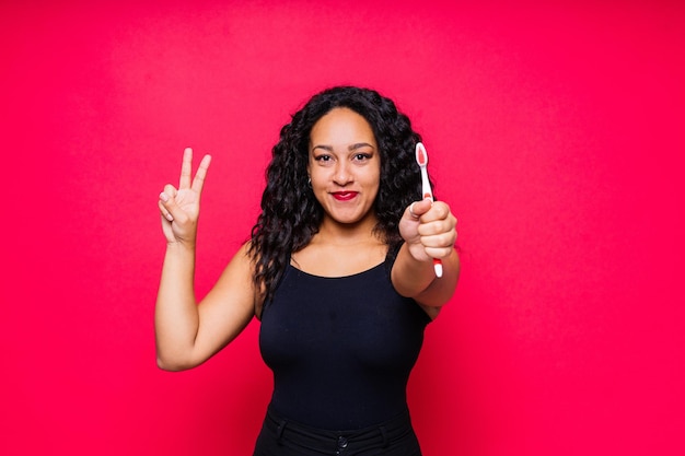 Mulher afro-americana feliz escova os dentes conceito de higiene dental isolado em fundo vermelho