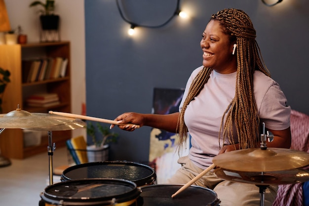 Mulher afro-americana feliz tocando bateria durante a repetição no estúdio musical