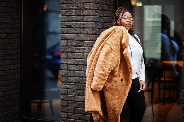 Mulher afro-americana glamorosa com casaco de pele quente, óculos posam na rua.