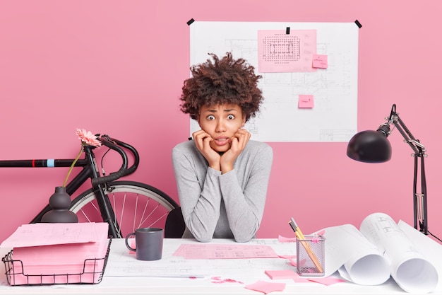 Foto mulher afro-americana intrigada e nervosa sentada no local de trabalho, trabalhando em um projeto de inicialização, vestida de maneira casual e desenhando esboços