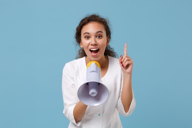 Mulher afro-americana médica isolada em fundo azul. Doutor em vestido médico branco segurando o dedo com nova ideia gritar no megafone. Conceito de medicina pessoal de saúde. Simule o espaço da cópia.