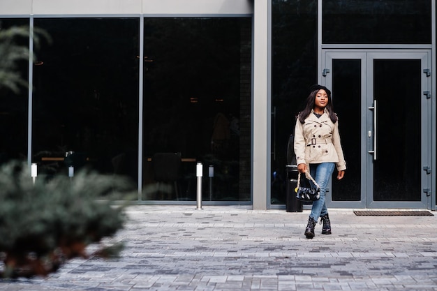 Mulher afro-americana na moda usar boina e casaco com bolsa posando ao ar livre.