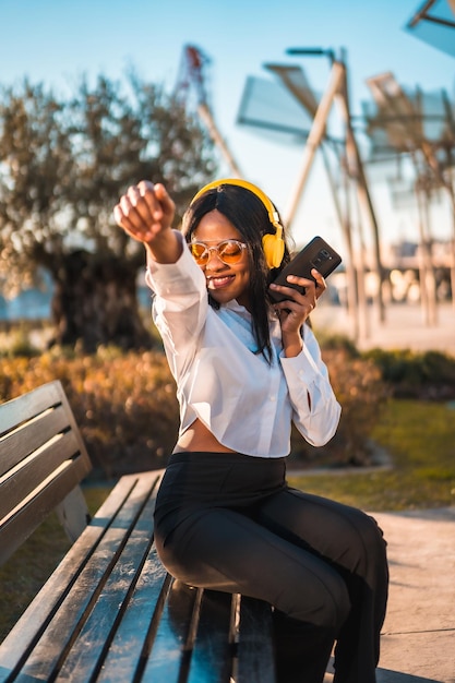 Mulher afro-americana ouvindo música com fones de ouvido ao pôr do sol em um parque dançando sorrindo