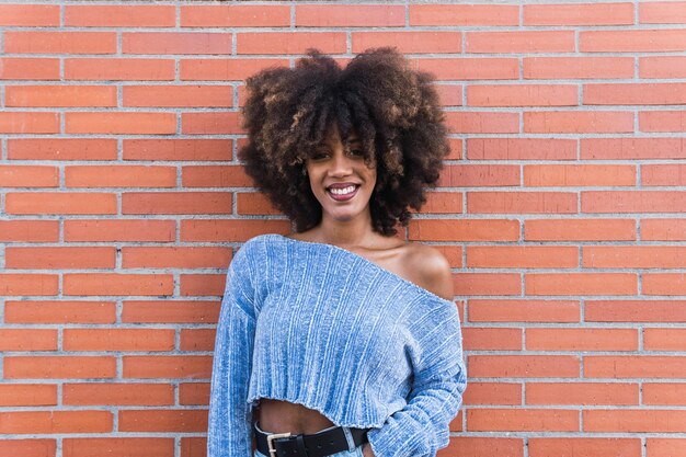 Foto mulher afro-americana positiva com cabelo longo afro maquiagem glamour e jumper azul em parede de tijolos