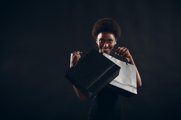 Mulher afro-americana segura sacolas de compras pretas Venda e descontos no mercado e no conceito de Black Friday