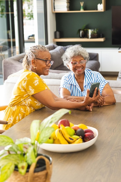 Mulher afro-americana sênior e mulher biracial sénior compartilham um momento em um smartphone em casa
