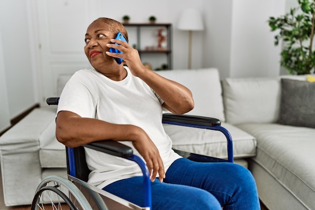 Mulher afro-americana sênior falando no smartphone sentado na cadeira de rodas em casa