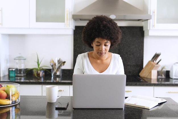 Mulher afro-americana sentada na cozinha usando laptop