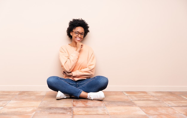 Foto mulher afro-americana sentada no chão com óculos e sorrindo