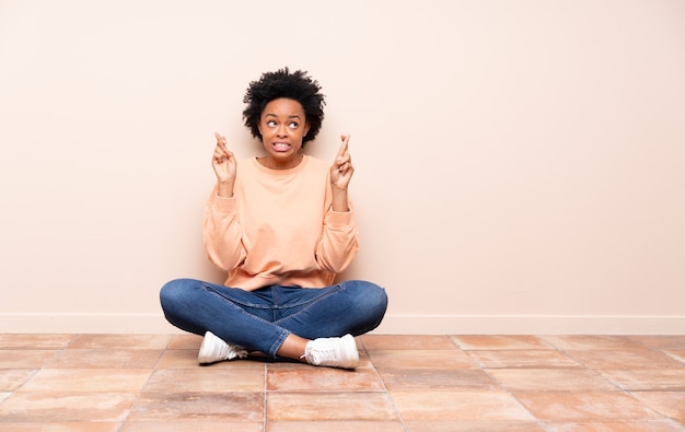 Mulher afro-americana sentada no chão com os dedos cruzados e desejando o melhor