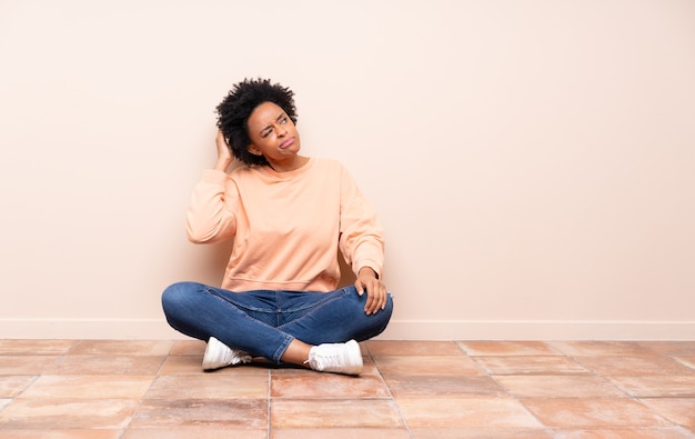 Mulher afro-americana sentada no chão tendo dúvidas enquanto coça a cabeça