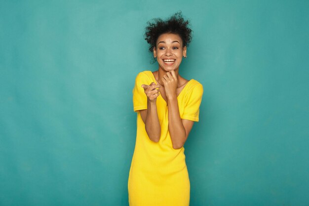 Mulher afro-americana sorridente apontando para a câmera, no fundo azul do estúdio, copie o espaço