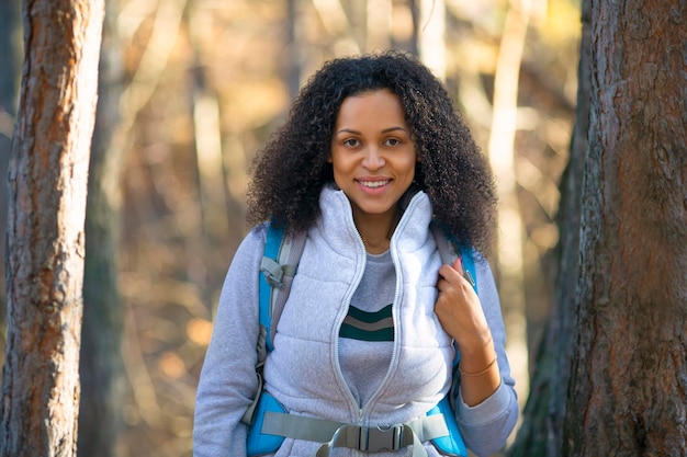 Mulher afro-americana sorridente com mochila em uma floresta