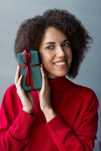 Mulher afro-americana sorridente de cabelos encaracolados segurando aniversário de comemoração de caixa de presentes em casa Feriados