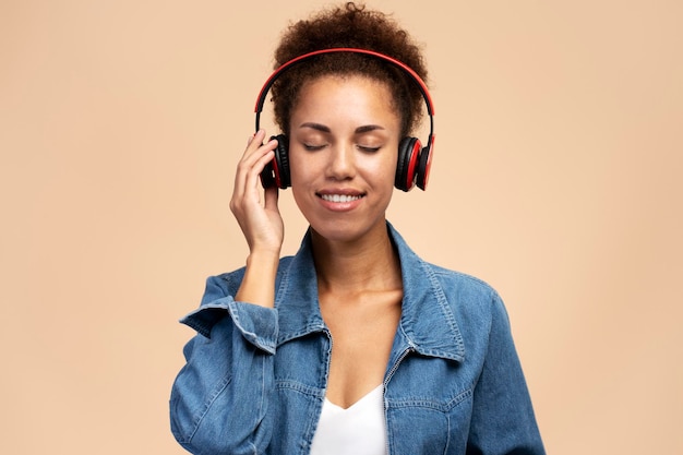 Mulher afro-americana sorridente ouvindo música com os olhos fechados em fones de ouvido sem fio