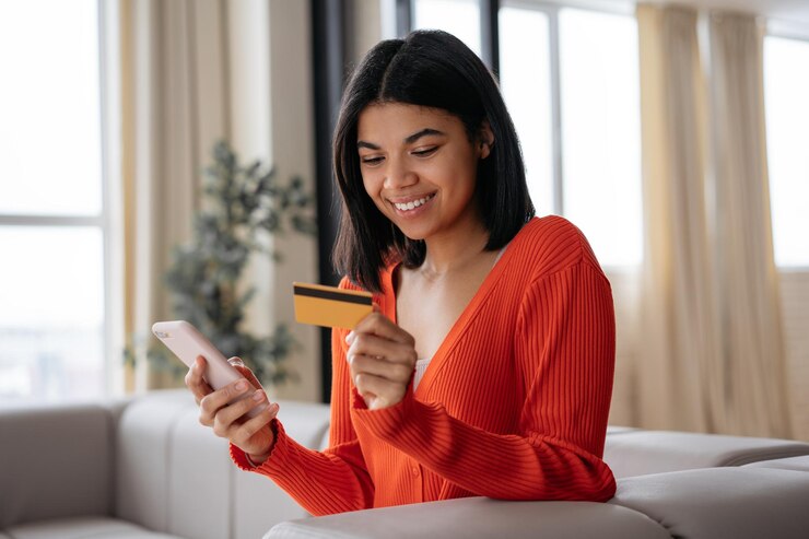 Foto mulher afro-americana sorridente segurando cartão de crédito usando telefone celular fazendo compras on-line em casa