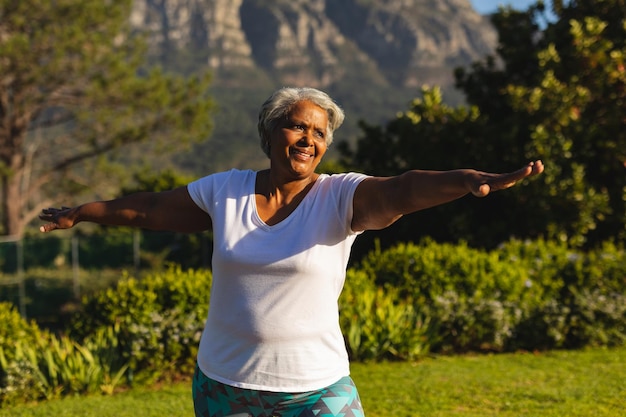 Foto mulher afro-americana sorridente sênior praticando ioga em uma paisagem deslumbrante. aposentadoria e conceito de estilo de vida sênior ativo.