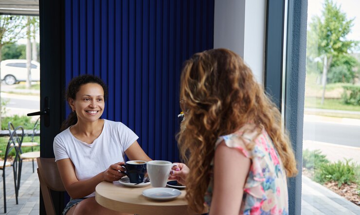 Foto mulher afro-americana sorridente, sentado à mesa em um café e conversando com seu amigo europeu durante uma xícara de café. garotas descansando em um café