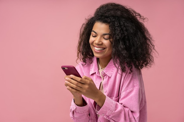 Foto mulher afro-americana sorridente usando smartphone jogando jogo para celular isolado em fundo rosa