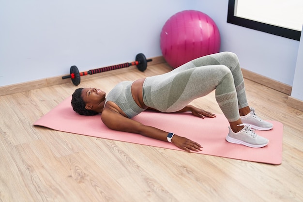 Mulher afro-americana sorrindo confiante treinando exercícios abdominais no centro esportivo