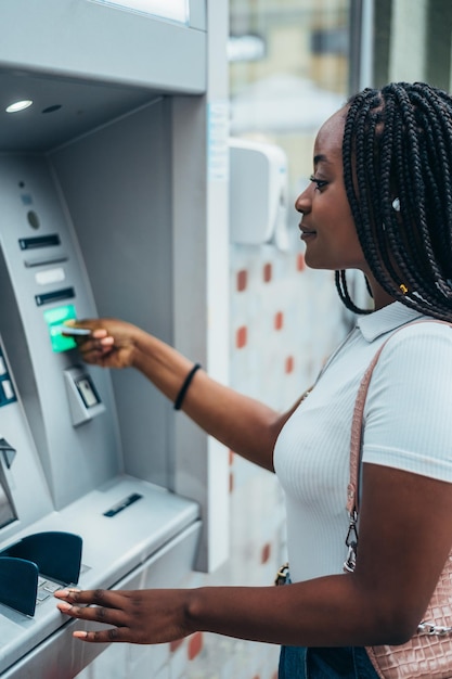 Mulher afro-americana usando cartão de crédito e sacando dinheiro no caixa eletrônico