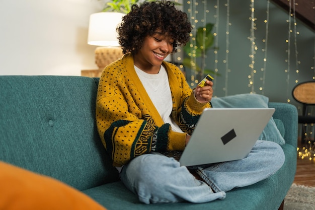 Mulher afro-americana usando laptop comprando on-line pagando com cartão de crédito de ouro garota sentada em