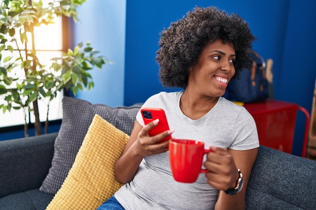 Mulher afro-americana usando smartphone bebendo café em casa