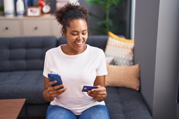 Mulher afro-americana usando smartphone e cartão de crédito sentado no sofá em casa