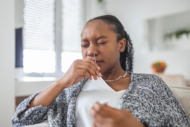 Foto mulher afro-americana usando um cotonete enquanto faz um teste pcr de coronavírus em casa mulher usando um teste de diagnóstico rápido de coronavírus mulher jovem em casa usando um cottonete nasal para covid-19