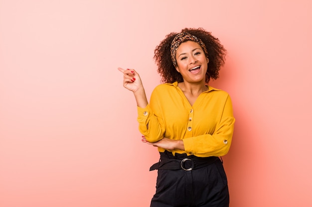 Mulher afro-americano nova contra um rosa que sorri alegremente apontando com o dedo indicador afastado.