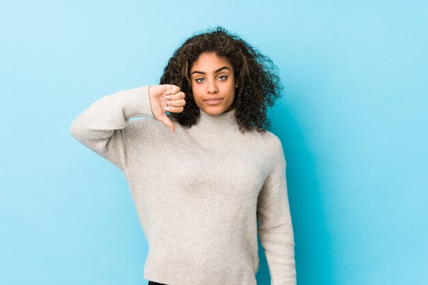 Mulher afro-americano nova do cabelo encaracolado que mostra um gesto do desagrado, polegares para baixo. Conceito de desacordo.