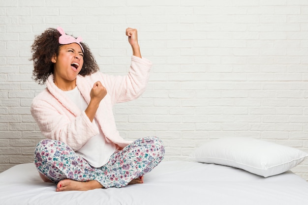 Mulher afro-americano nova na cama que veste o pijama que levanta o punho após uma vitória, conceito do vencedor.