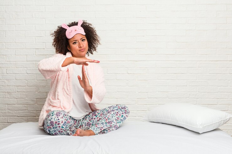 Foto mulher afro-americano nova na cama que veste o pijama que mostra um gesto do intervalo.
