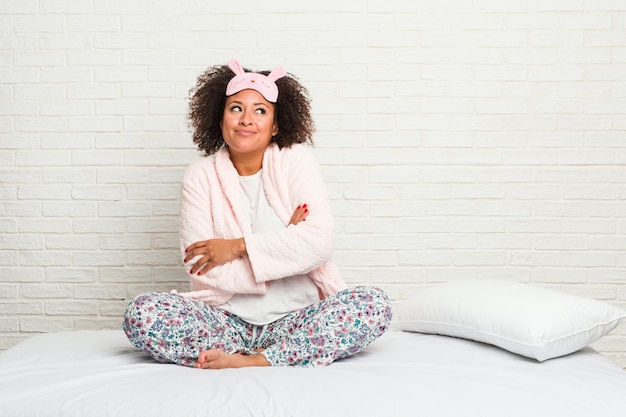 Mulher afro-americano nova na cama que veste o sorriso do pijama seguro com braços cruzados.