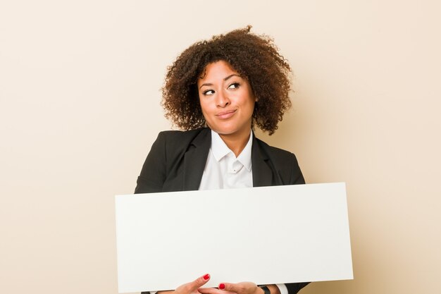 Mulher afro-americano nova que mantém um sorriso do cartaz seguro com braços cruzados.