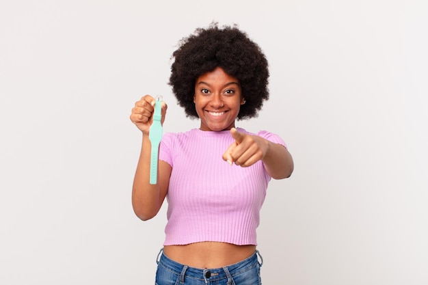 Mulher afro apontando para a câmera com um sorriso satisfeito, confiante e amigável, escolhendo o conceito de seu relógio