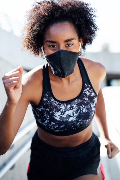 Mulher afro-atlética usando máscara facial enquanto corre ao ar livre