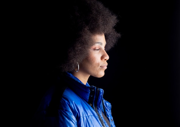 Mulher afro bem mesclada, sorridente, com roupas urbanas sérias, olhar triste, na superfície escura