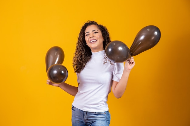 Mulher afro com balões pretos, comemorando ofertas de aniversário. Vendas da Black Friday