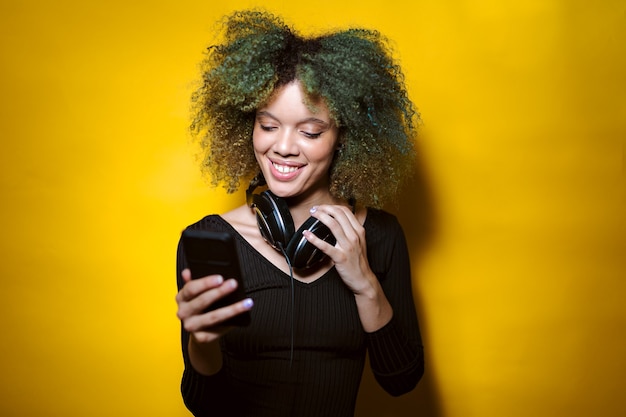 Mulher afro com telefone celular e fones de ouvido em fundo amarelo