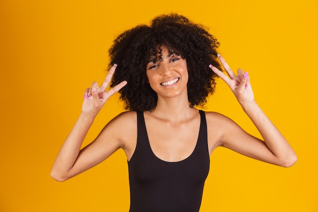 Mulher afro fazendo sinal de V com as mãos. Garota afro feliz com boa vibração fazendo paz e amor com as mãos