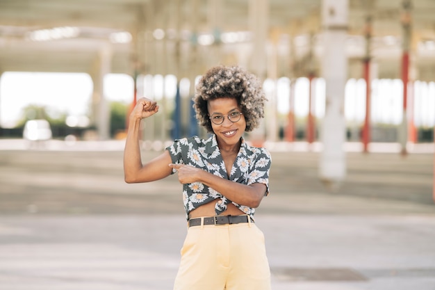 Mulher afro feliz em pé, apontando o braço esticando-se em uma rua urbana