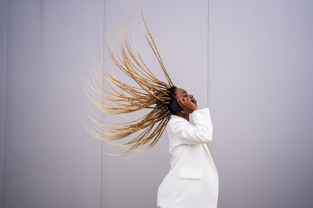 Mulher afro movendo o cabelo para trás enquanto conversa com o celular ao ar livre